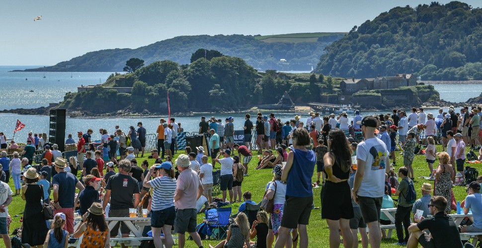 Crowds of Plymouth sat on Plymouth Hoe on a sunny day, looking out to sea as SailGP takes place